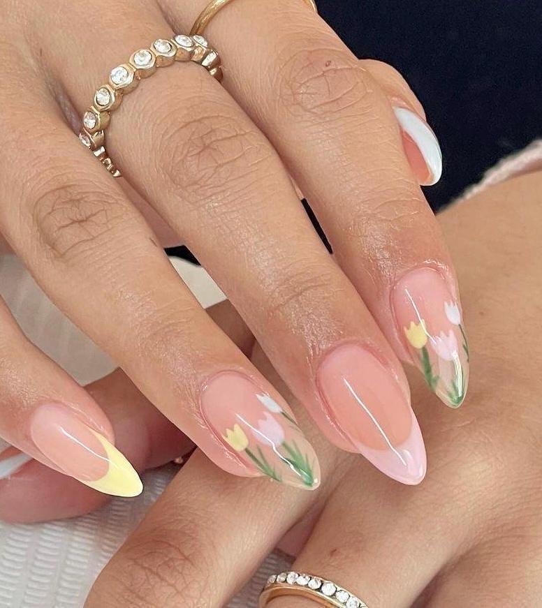 May include: Almond shaped nails with a light pink base and a white tip. The nails are decorated with a floral design of white and yellow tulips with green leaves.